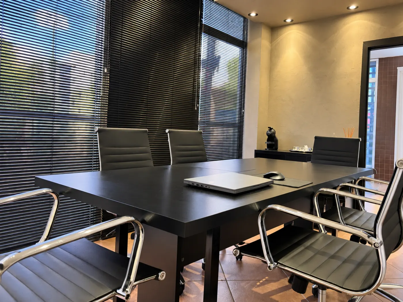 Sala de reuniões com mesa retangular preta, cadeiras de couro, notebook sobre a mesa e iluminação embutida